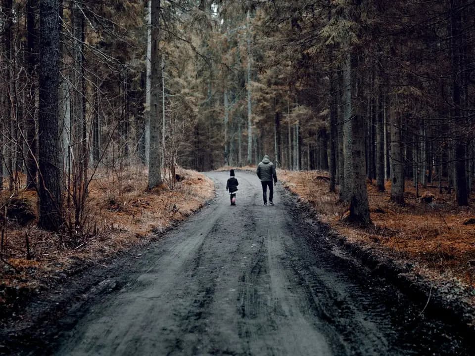 Barn og voksen på skogstur langs grusvei